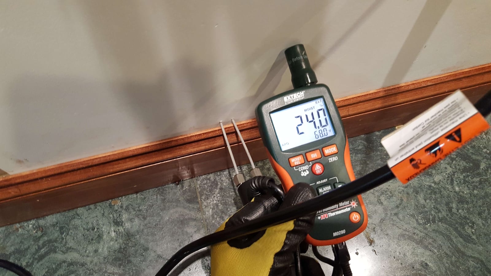 Extech pin-type moisture meter showing 24% reading at a wet baseboard during water damage inspection