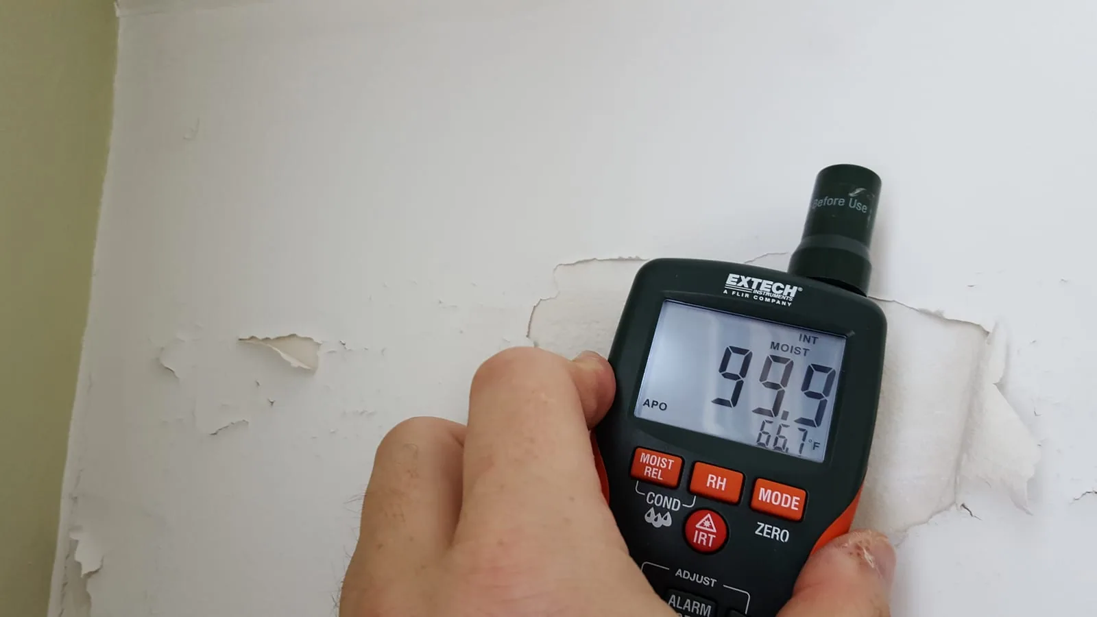 Moisture meter detecting hidden water damage behind peeling paint