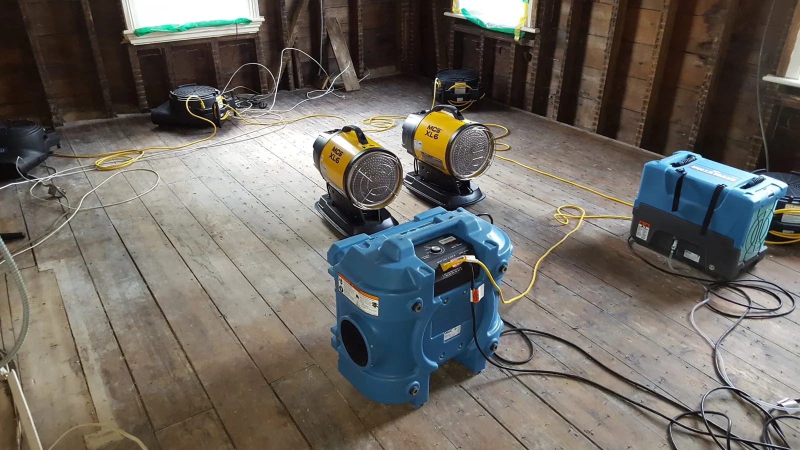 Industrial air movers, heaters, and a dehumidifier drying a gutted room down to the studs